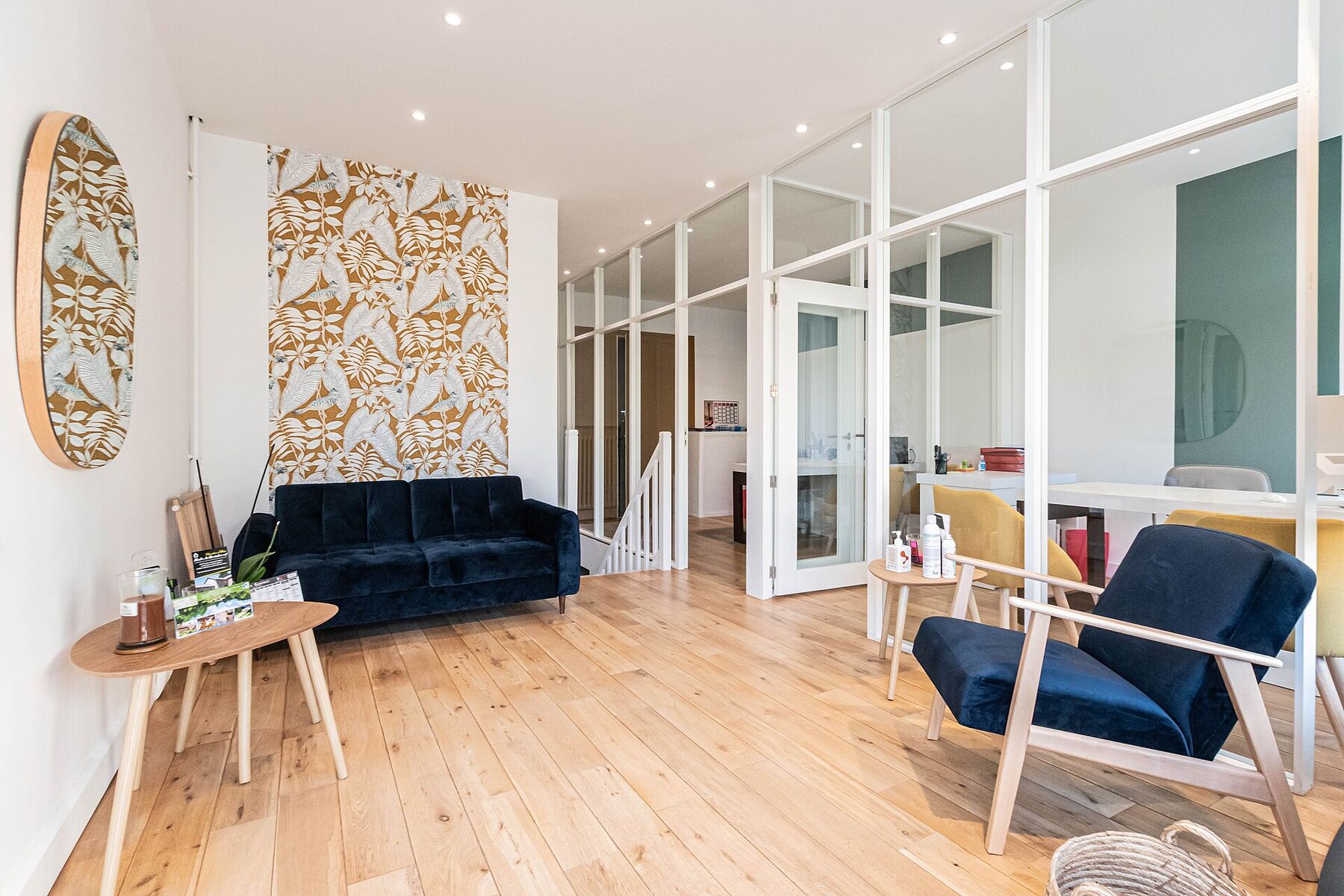 Intérieur clair d'une agence immobilière : parquet, fauteuils d'accueil, bureaux derrière des cloisons vitrées