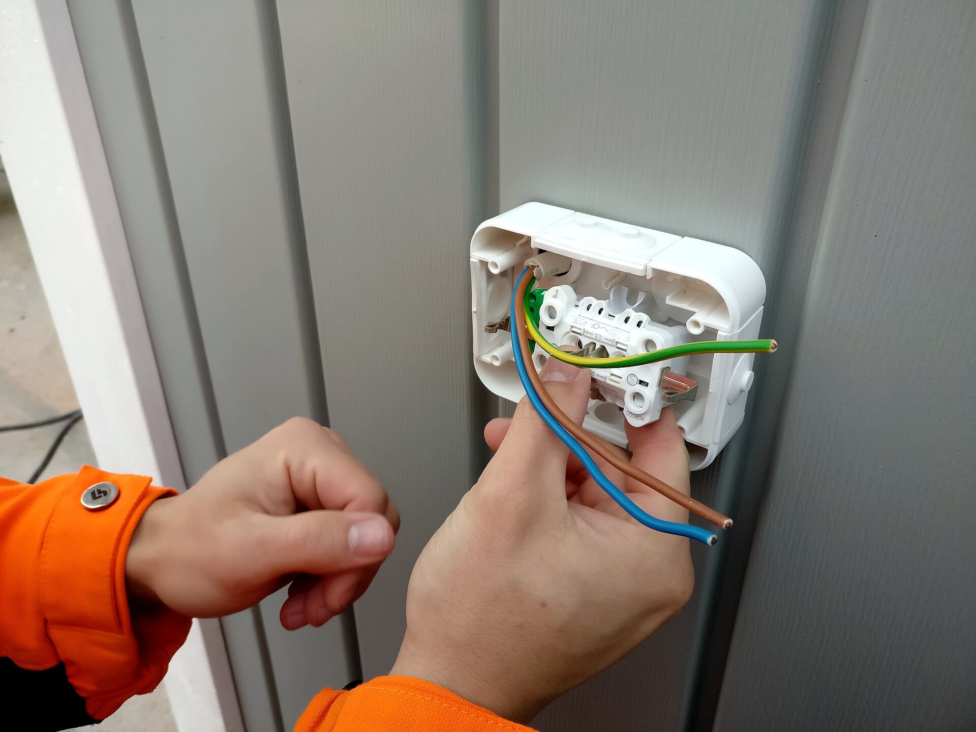 Mains d'un électricien qui raccorde les fils d'une prise murale