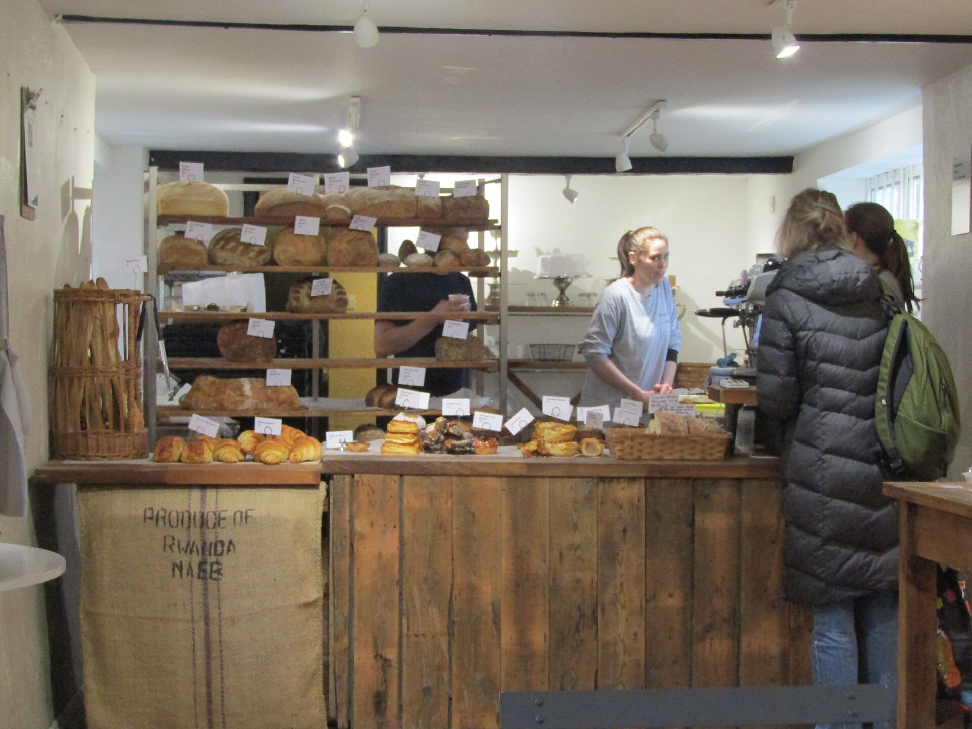 Comptoir en bois d'une boulangerie indépendante, pains sur les étagères, une vendeuse sert des clientes
